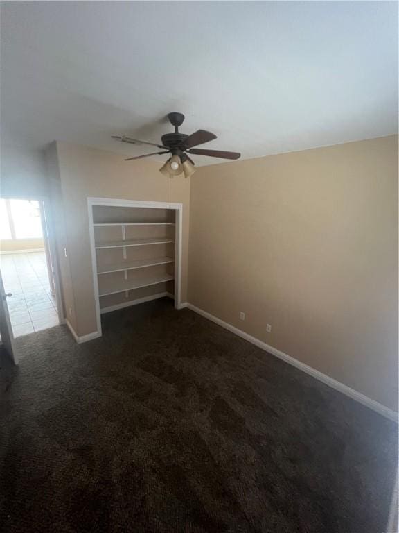 unfurnished bedroom with dark colored carpet, a closet, and ceiling fan