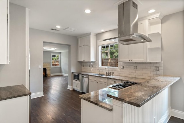 kitchen with dark stone counters, kitchen peninsula, built in microwave, island range hood, and white cabinetry