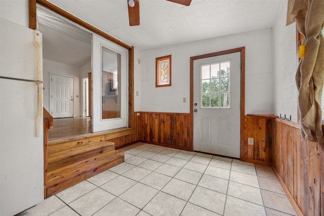 entryway with ceiling fan, light tile patterned floors, and wood walls