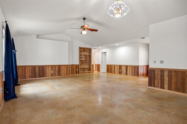 spare room featuring ceiling fan with notable chandelier, wooden walls, and vaulted ceiling