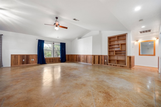 empty room featuring built in shelves, ceiling fan, wood walls, vaulted ceiling, and a textured ceiling