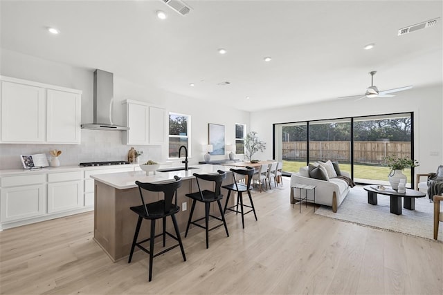 kitchen featuring white cabinets, sink, wall chimney range hood, and an island with sink