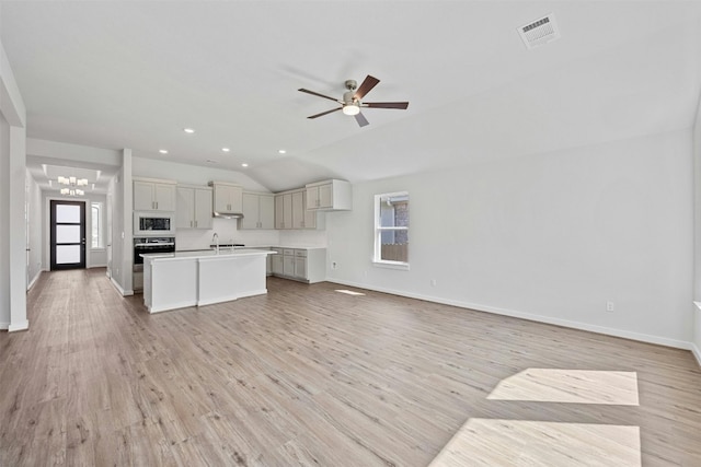 kitchen with stainless steel oven, an island with sink, light hardwood / wood-style floors, vaulted ceiling, and white microwave