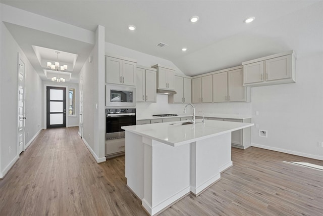 kitchen featuring built in microwave, an inviting chandelier, light hardwood / wood-style flooring, oven, and a center island with sink