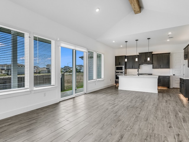 kitchen with an island with sink, open floor plan, hanging light fixtures, stainless steel appliances, and light countertops