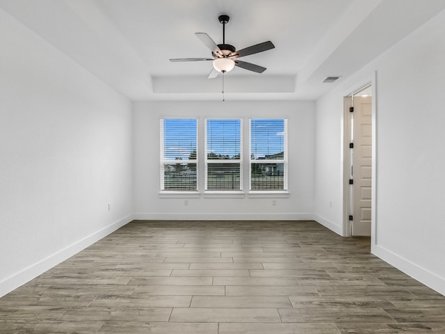 unfurnished room featuring light hardwood / wood-style flooring, a tray ceiling, and ceiling fan