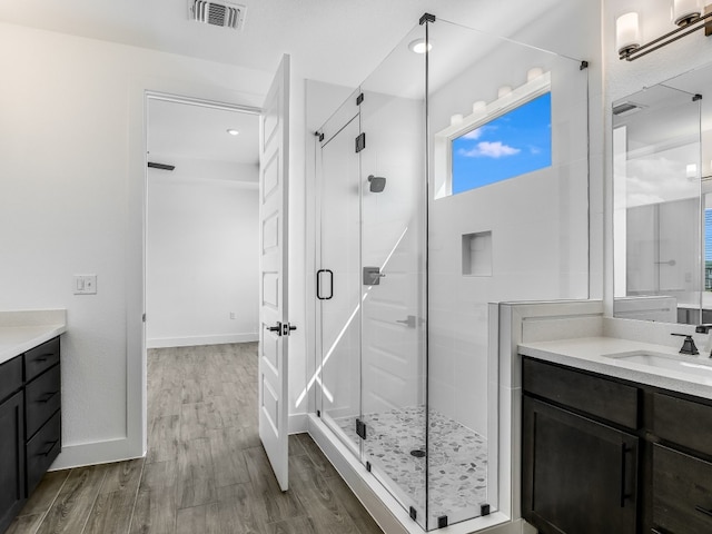 full bathroom with visible vents, vanity, a shower stall, wood finished floors, and baseboards