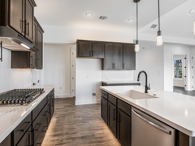 kitchen featuring a kitchen island with sink, dark wood-type flooring, stainless steel appliances, sink, and decorative light fixtures