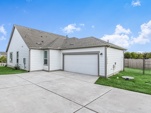 exterior space with an attached garage, a shingled roof, fence, and a lawn