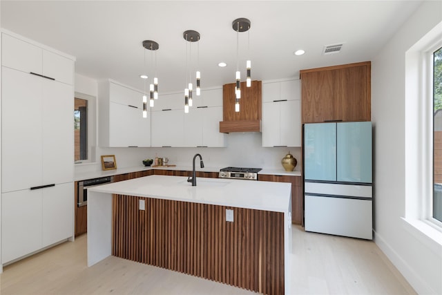 kitchen with white cabinets, light hardwood / wood-style flooring, hanging light fixtures, refrigerator, and a center island with sink