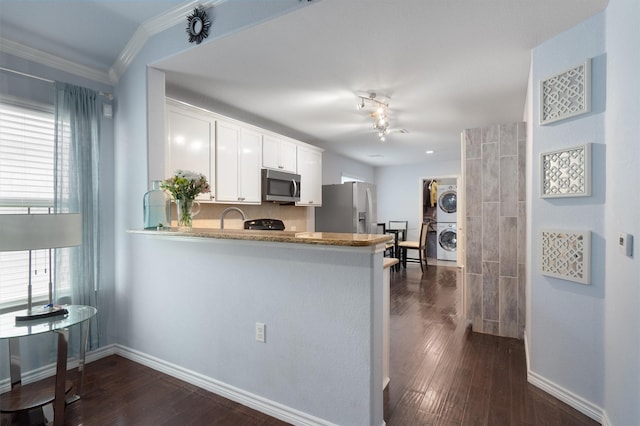 kitchen with white cabinetry, stacked washer / drying machine, kitchen peninsula, appliances with stainless steel finishes, and crown molding