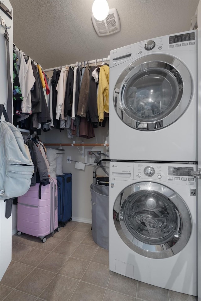 laundry area with a textured ceiling, stacked washer and dryer, and tile patterned flooring