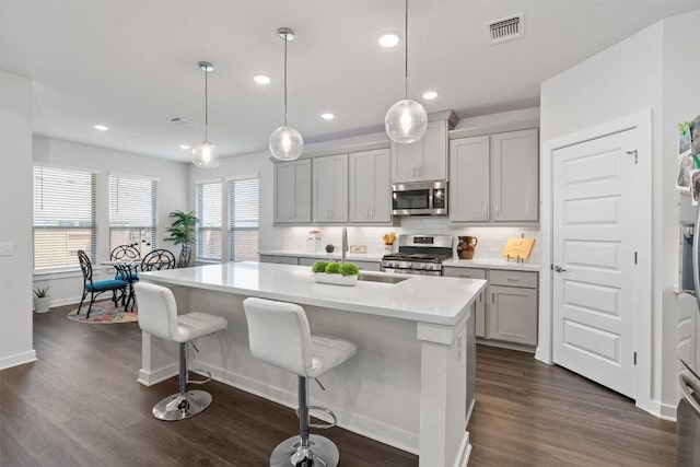 kitchen featuring stainless steel appliances, decorative light fixtures, a center island with sink, and gray cabinetry