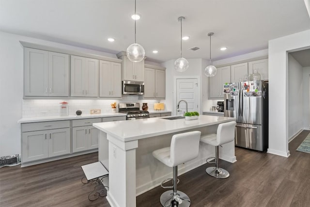 kitchen featuring stainless steel appliances, an island with sink, hanging light fixtures, and a kitchen breakfast bar