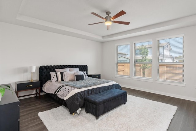 bedroom with ceiling fan, dark hardwood / wood-style flooring, and a tray ceiling