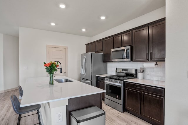 kitchen featuring an island with sink, a breakfast bar area, decorative backsplash, appliances with stainless steel finishes, and light wood-type flooring