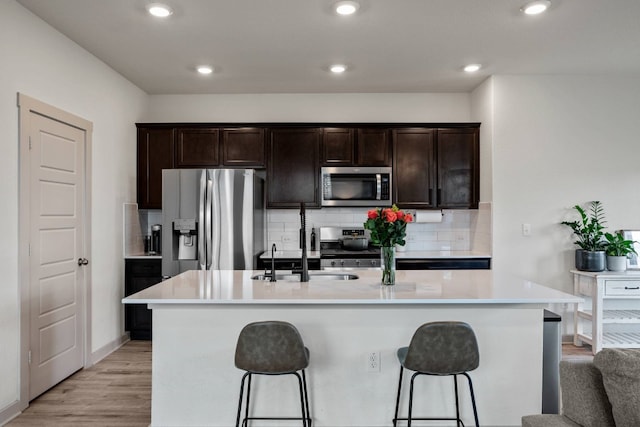 kitchen featuring a center island with sink, light hardwood / wood-style floors, stainless steel appliances, and tasteful backsplash