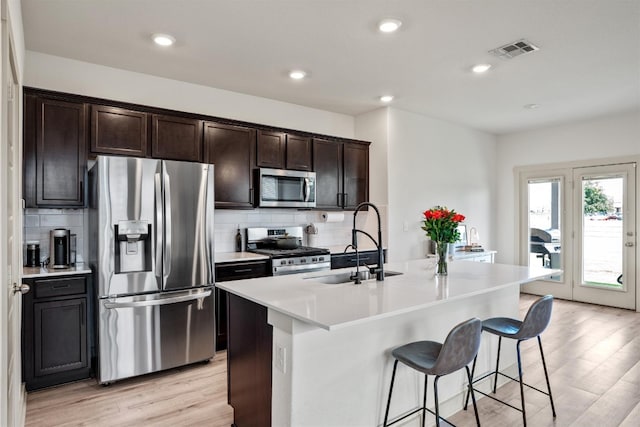 kitchen with stainless steel appliances, sink, light hardwood / wood-style floors, a breakfast bar area, and an island with sink