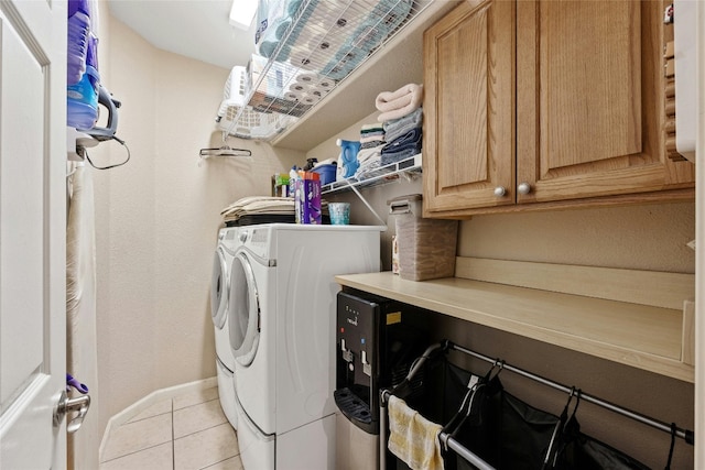 clothes washing area featuring washer and dryer, light tile patterned floors, and cabinets