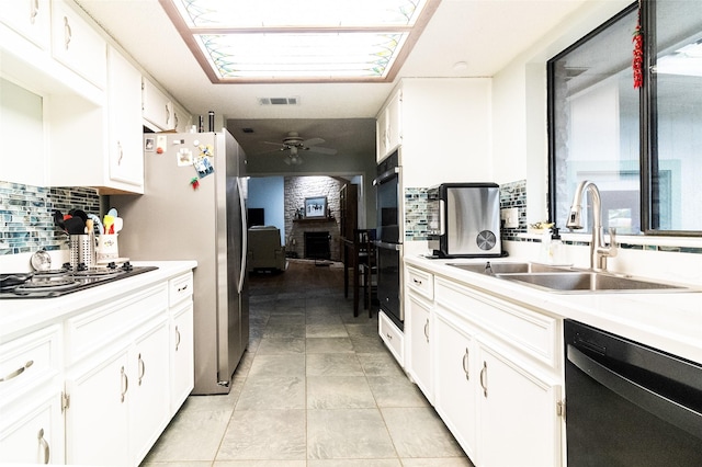 kitchen with a large fireplace, sink, white cabinets, backsplash, and stainless steel appliances