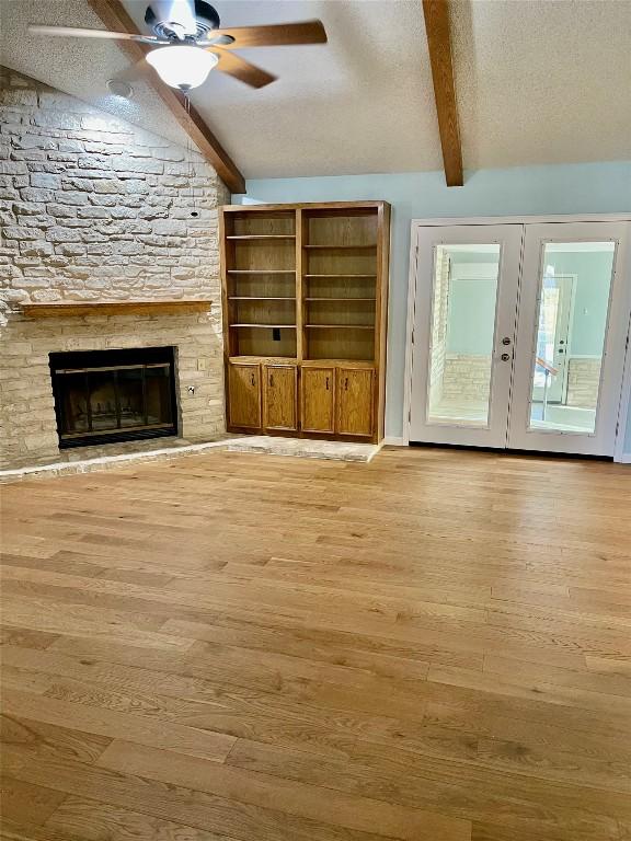 unfurnished living room featuring a fireplace, lofted ceiling with beams, ceiling fan, a textured ceiling, and light wood-type flooring