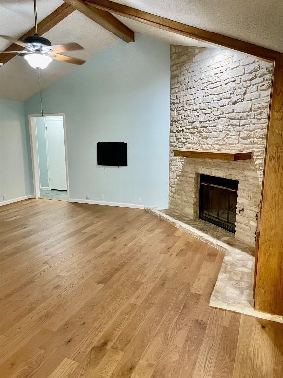 unfurnished living room featuring a fireplace, vaulted ceiling with beams, light wood-type flooring, ceiling fan, and a textured ceiling