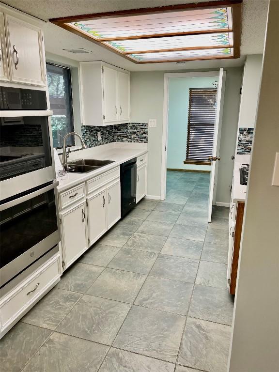 kitchen featuring sink, dishwasher, double oven, tasteful backsplash, and white cabinets