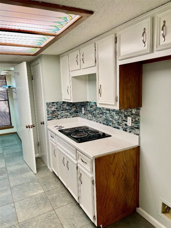 kitchen with tasteful backsplash, black electric stovetop, light stone countertops, and white cabinets