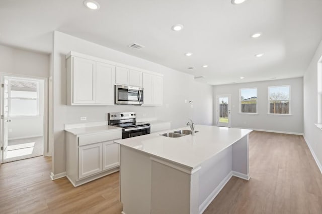 kitchen featuring sink, white cabinets, light hardwood / wood-style floors, stainless steel appliances, and a center island with sink