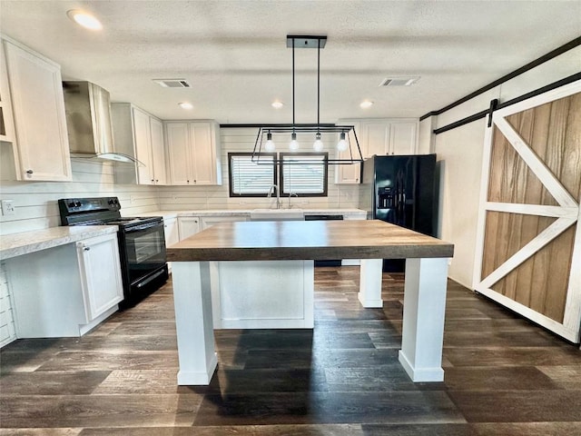 kitchen with wall chimney exhaust hood, decorative light fixtures, black appliances, a barn door, and white cabinets