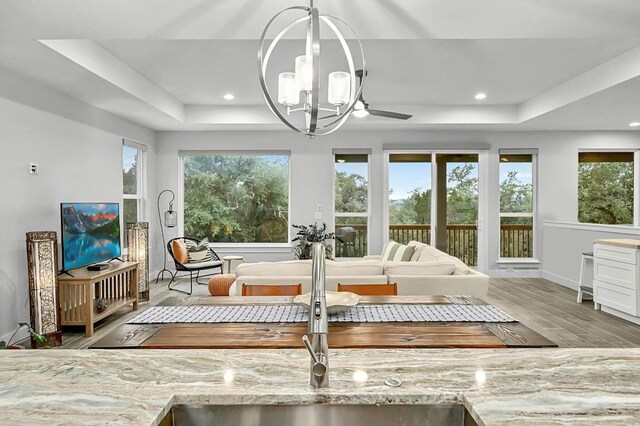 sunroom / solarium with ceiling fan with notable chandelier, a tray ceiling, and sink