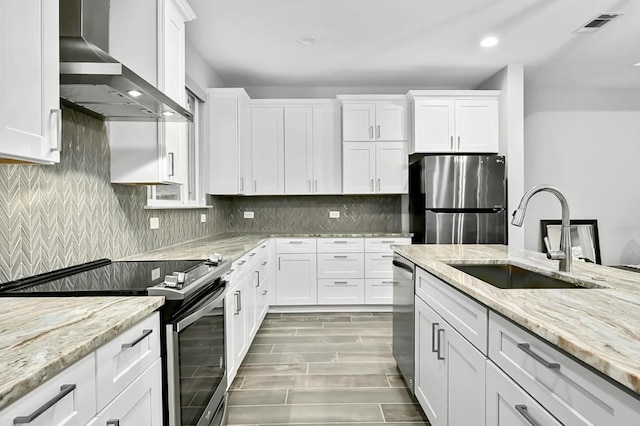 21201 Norris Cv, Lago Vista, TX 78645 - kitchen featuring wall chimney range hood, appliances with stainless steel finishes, a sink, white cabinetry, and light stone counters