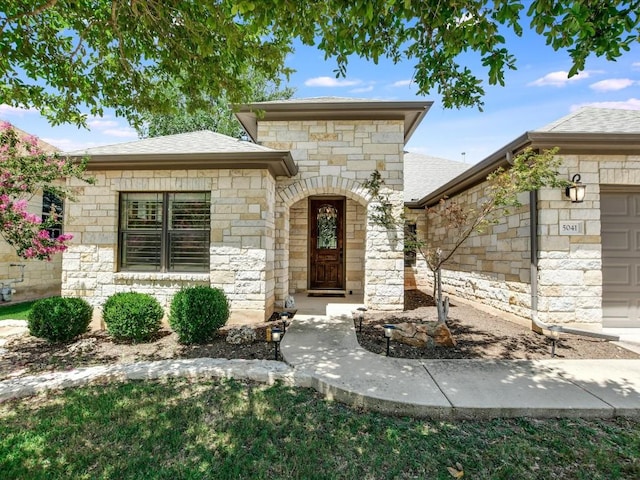 doorway to property featuring stone siding, a garage, and roof with shingles