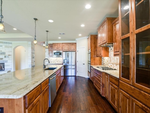 kitchen featuring appliances with stainless steel finishes, a sink, arched walkways, light stone countertops, and tasteful backsplash