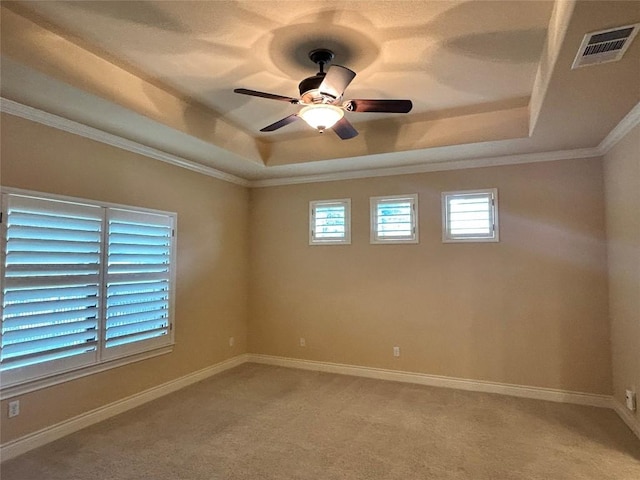 spare room with a raised ceiling, a ceiling fan, healthy amount of natural light, crown molding, and light colored carpet