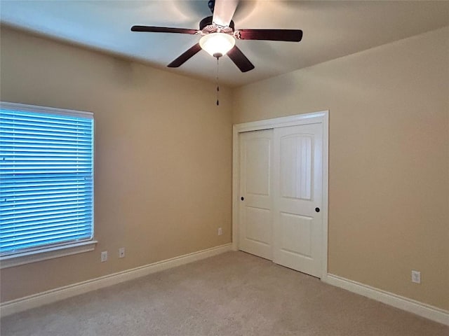 unfurnished bedroom featuring light colored carpet, a closet, baseboards, and ceiling fan
