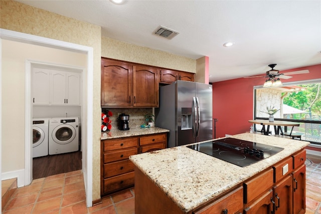 kitchen featuring washing machine and dryer, black electric cooktop, visible vents, stainless steel fridge with ice dispenser, and a center island