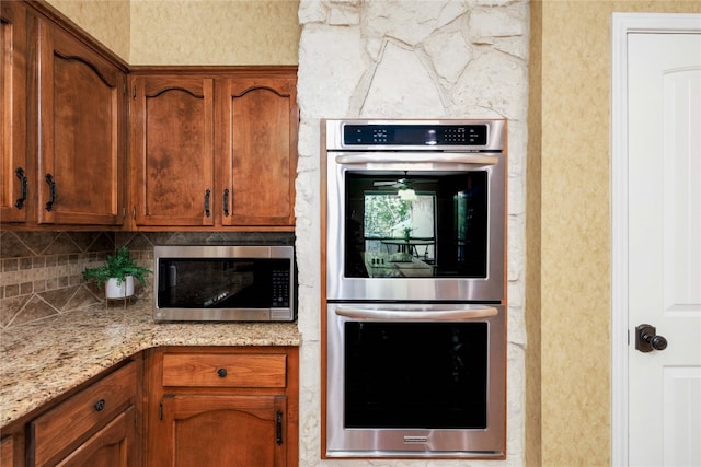 kitchen featuring light stone countertops, appliances with stainless steel finishes, brown cabinets, and backsplash