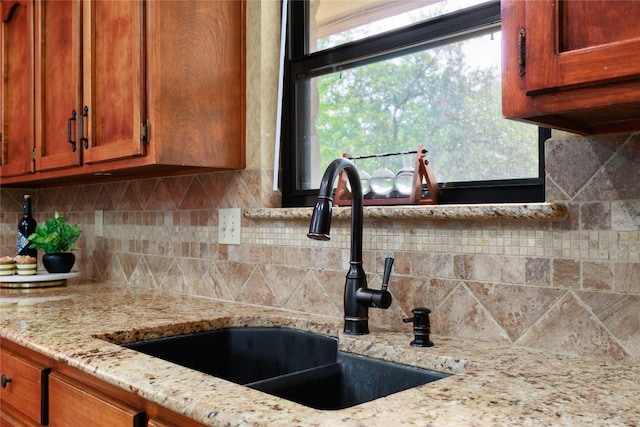 kitchen with light stone counters, backsplash, a sink, and brown cabinets