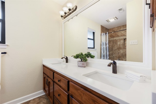 bathroom with double vanity, visible vents, a tile shower, and a sink