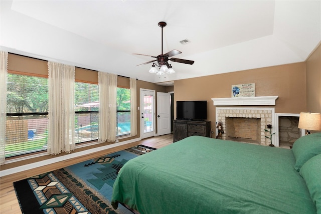 bedroom with a ceiling fan, a brick fireplace, visible vents, and wood finished floors