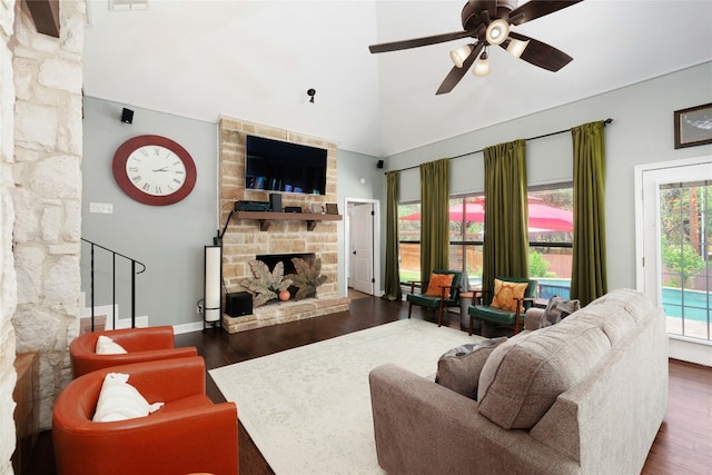 living area with ceiling fan, a fireplace, wood finished floors, and a towering ceiling