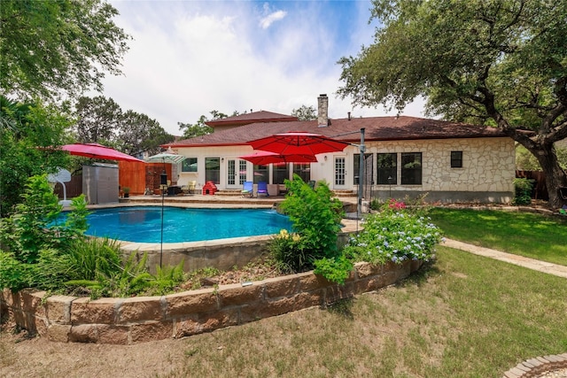 outdoor pool featuring a patio area, an outdoor structure, a lawn, and french doors