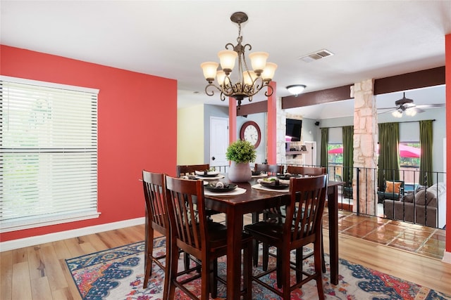 dining space featuring ceiling fan with notable chandelier, wood finished floors, visible vents, baseboards, and decorative columns