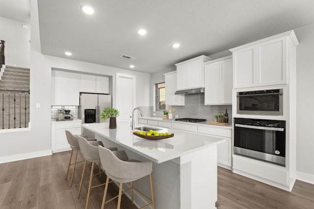 kitchen with stainless steel appliances, white cabinetry, a center island with sink, and sink