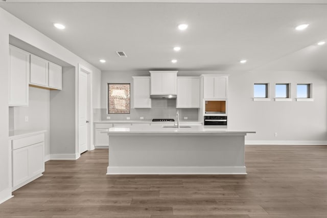 kitchen featuring stainless steel oven, sink, dark wood-type flooring, a kitchen island with sink, and white cabinets