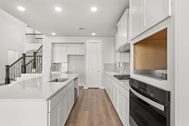 kitchen featuring stainless steel appliances, a kitchen island with sink, sink, wood-type flooring, and white cabinets