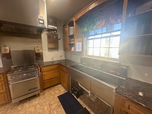 kitchen featuring stainless steel range, range hood, dark stone countertops, and light tile floors