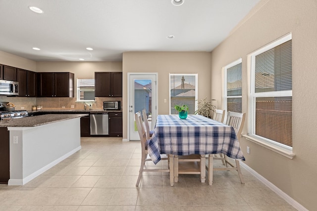 interior space with stainless steel appliances, dark brown cabinets, tasteful backsplash, light tile patterned floors, and dark stone counters