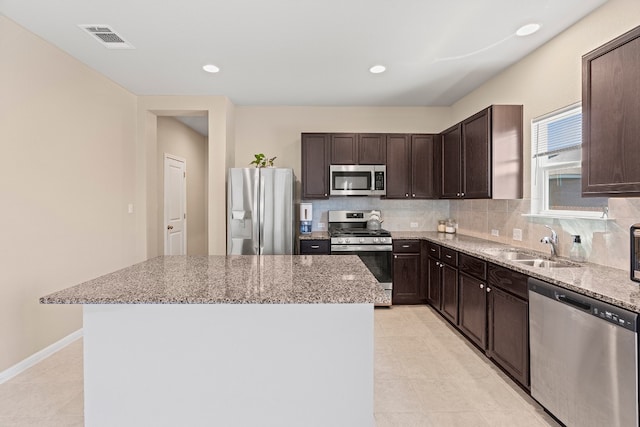 kitchen featuring light tile patterned floors, stainless steel appliances, light stone counters, and a kitchen island